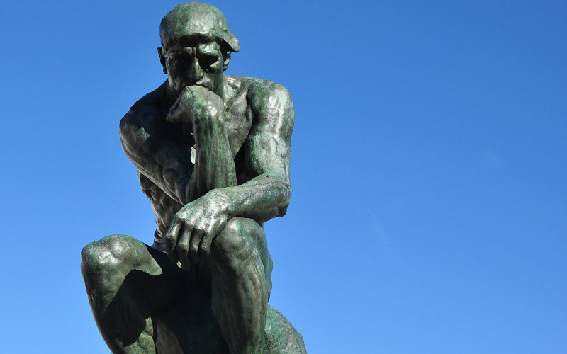 Fotografia mostra sobre fundo de céu azul a estátua do Pensador, de Auguste Rodin, simbolizando o pensamento e remetendo aos gatilhos mentais.