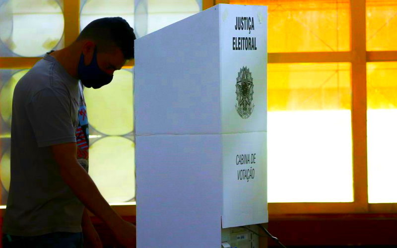 Foto de Marcelo Camargo, da Agência Brasil, mostra homem de pé, em frente a uma cabine de votação, fazendo as suas escolhas nas eleições.