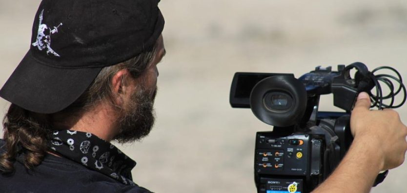 Imagem mostra homem operando câmera profissional de gravação de conteúdo político em vídeo.