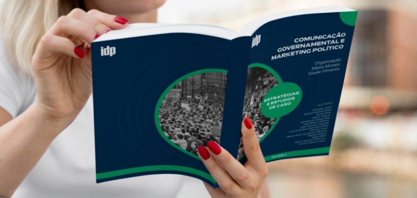 Imagem mostra mulher sentada num sofá, lendo o segundo volume do livro Comunicação Governamental e Marketing Político, com capa predominantemente azul e o nome dos autores e das organizadoras.