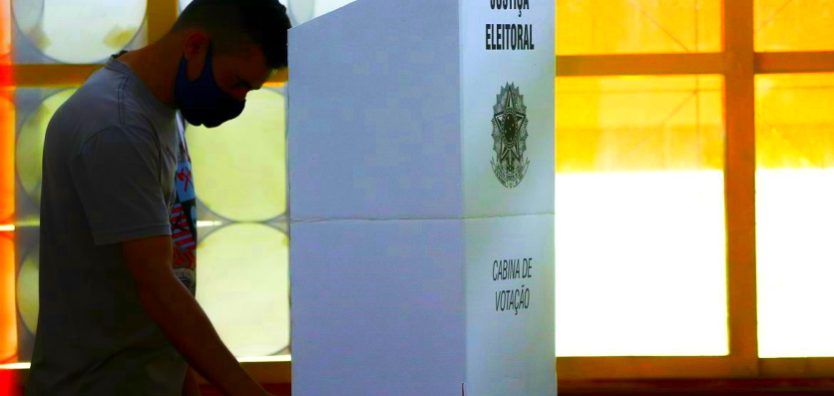 Foto de Marcelo Camargo, da Agência Brasil, mostra homem de pé, em frente a uma cabine de votação, fazendo as suas escolhas nas eleições.